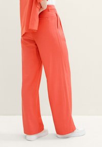 Coral wide-leg trousers made from lightweight fabric, featuring a smooth texture and side pockets, paired with white sneakers.