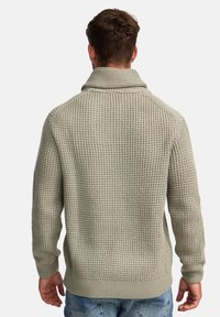 Suéter de punto en gris claro con patrón texturizado, con un cuello alto y puños acanalados. Mangas de longitud media y aberturas laterales en el dobladillo.