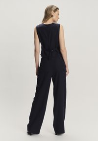 Námornícky bezramenný top s peplum lemem a zavazováním na zádech. Spárován s volnými kalhotami, obojí ve strukturované tkanině.
