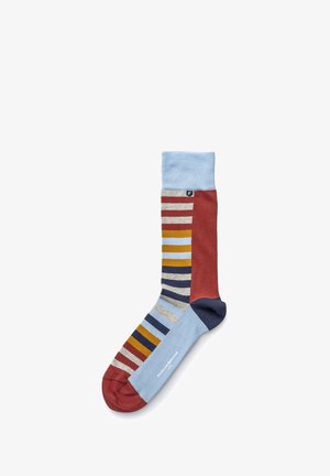 Chaussette multicolore avec une combinaison de rayures bleues, rouges et grises, dotée d'un poignet côtelé. Le tissu semble doux et texturé, avec des détails de logo.