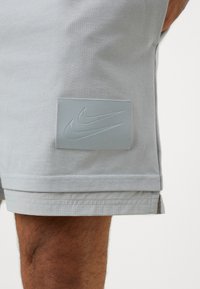 Light gray shorts made of cotton blend, featuring a textured Nike logo patch. The hem is double-stitched with small perforations.