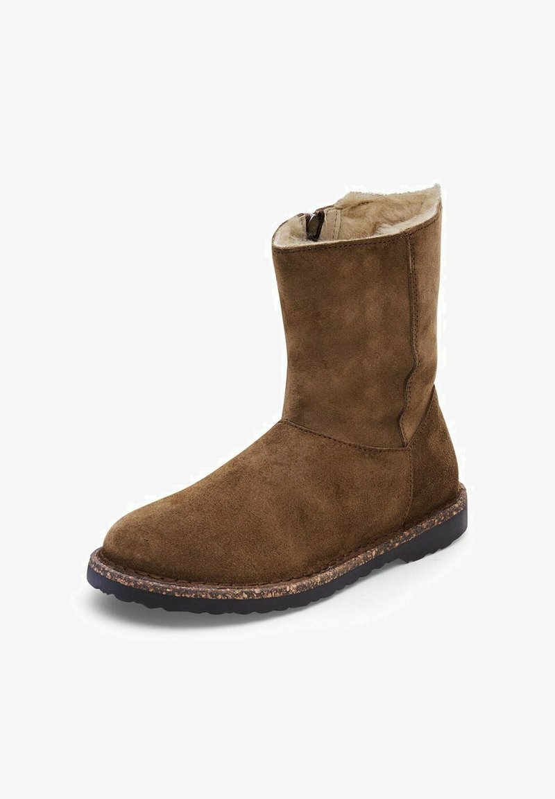 Bottes en daim marron à cheville avec une doublure en fourrure douce, texture lisse, bout arrondi et semelle en caoutchouc texturée pour l'adhérence. Fermeture éclair sur le côté.