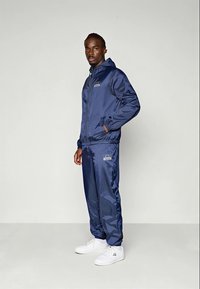 Navy blazer trainingspak van lichtgewicht, glanzend materiaal; bevat een ritsjack, elastische manchetten en bijpassende broeken met logodetails.
