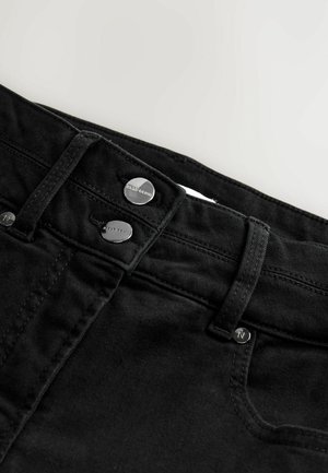 Černé džínové kalhoty mají hladkou texturu, dva stříbrné knoflíky na pase a klasický pětikusový design.