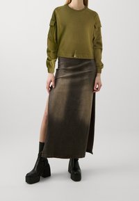 Sweat-shirt court vert olive avec poignets côtelés et poches latérales, associé à une longue jupe dégradée marron avec une fente latérale et des bottines à plateforme noires.