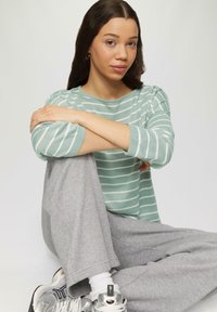 Lichtgroen gestreepte trui met lange mouwen, gecombineerd met losse grijs geruite pyjamabroek en metallic sneakers.