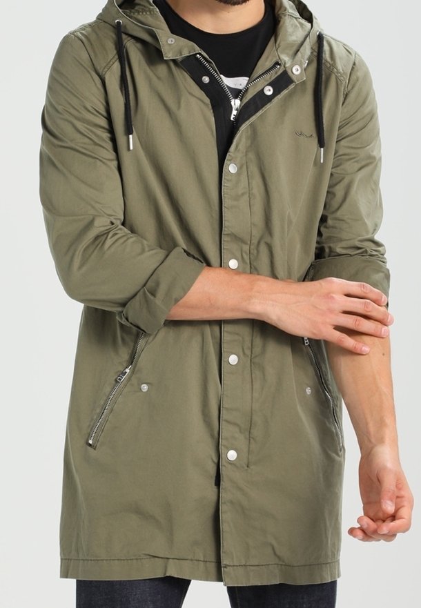 Veste à capuche vert olive avec détails de fermeture éclair argentée, boutons-pression et poches latérales. Fabriquée en tissu léger, avec cordons ajustables.