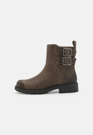 Brown leather ankle boot with a rounded toe, two adjustable buckles on the side, and a textured rubber sole for grip.