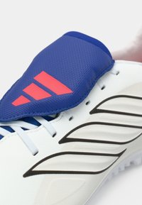 Valkoiset urheilukengät, joissa on sininen kangasosa ja punaiset yksityiskohdat. Ominaisuuksina teksturoitu muotoilu ja musta logo yksityiskohtana sivussa.