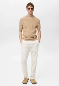 Pulover bej cu mânecă scurtă, pantaloni albi drepți și pantofi slip-on bej, asortați cu ochelari de soare rotunzi. Design simplu și modern.