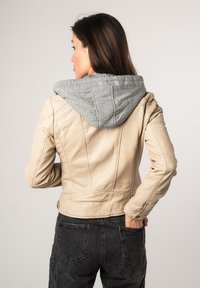 Beige leren jas met een grijze stoffen capuchon, aansluitend ontwerp, gladde textuur en stikdetails, gecombineerd met zwarte jeans.