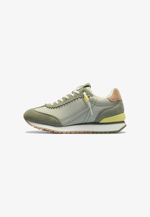 Zapatilla casual en verde apagado con paneles de ante y tela, cordones blancos, lengüeta del talón en marrón claro y suela bicolor con acento amarillo.