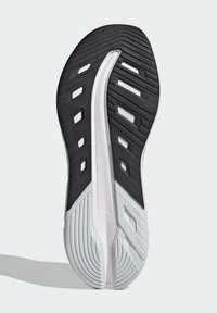 Schuhsohle mit einer schwarzen Gummi-Oberfläche und weißen Akzenten, strukturierten Mustern für besseren Grip und einer geschwungenen weißen Zwischensohle zur Dämpfung.