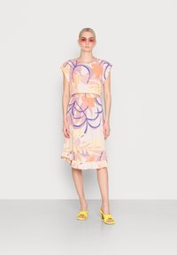 Vestido com padrão floral em tons pastel, com mangas curtas, cintura elástica e bainha com volantes. Combinado com sapatos de salto amarelos com nó.