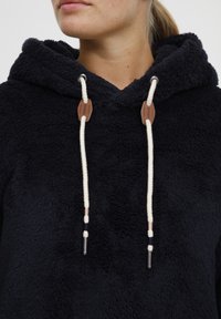 Navy fleece hoodie featuring a textured fabric, large hood, and contrasting white drawstrings with brown accents.