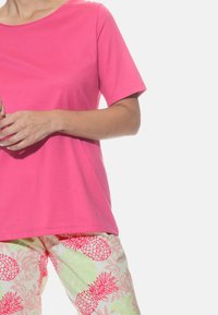 Kortærmet, rundhalset lyserød t-shirt parret med lette, mønstrede bukser med lyserøde ananaser på en lys baggrund.