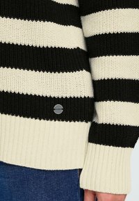 Maglione lavorato a maglia a strisce nere e crema con bordo e polsini a costine. Presenta un piccolo etichetta in argento sul lato. Vestibilità casual.