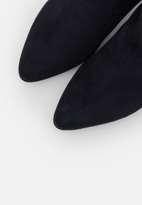 Bottines en daim bleu marine avec un bout pointu et une texture lisse. Présentent des coutures minimales et un design épuré sans éléments métalliques visibles.