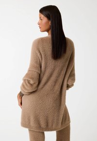 Maglione a maniche lunghe e taglio morbido, realizzato in un tessuto beige testurizzato, caratterizzato da una silhouette rilassata e cuciture delle spalle cadenti.
