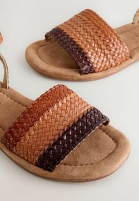 Tkané kožené skluzné sandály s pásky v odstínech tan, světle hnědé a tmavě hnědé. Měkká semišová stélka s zaobleným tvarem a minimálními kovovými prvky.