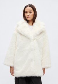 Λευκό παλτό από ψεύτικη γούνα με φαρδύ γιακά, μακριά μανίκια και άνετη εφαρμογή· διαθέτει απαλή, αφράτη υφή και κεντρικό κούμπωμα.