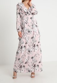 Abito lungo in tessuto rosa chiaro con motivo floreale nero, maniche arricciate e dettagli a strati. Presenta un profondo scollo a V.
