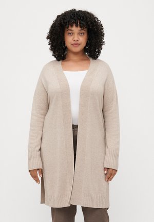 Lys beige cardigan, strikket stoff, åpen frontdesign, ribbede mansjetter og kant, faller til midt på lårene, brukt over en hvit topp og brune bukser.
