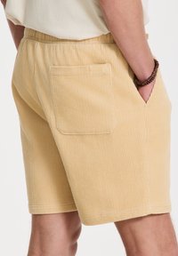 Korsettishorts i lys gul med ribbet tekstur, elastisk midjebånd og baklomme. Romslig passform og knelengde.