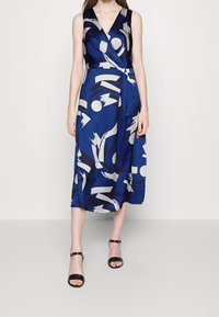Blue wrap dress with abstract white and dark blue patterns, v-neckline, sleeveless design, and flowing mid-length skirt.