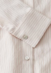 Lichtroze gestreept shirt met een knoopmanchet, zachte textuur en subtiele glans. Gemaakt van ademende stof met een klassiek kraagontwerp.