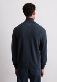 Dunkelblauer Strickpullover mit hohem Kragen, strukturiertem Muster und gerippten Bündchen; figurbetontes Design, das sich gut zum Schichten eignet.