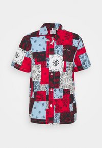 Camicia a maniche corte in cotone, caratterizzata da un design patchwork in rosso, blu, nero e bianco con motivi floreali e paisley.