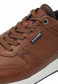 Sneaker en cuir marron avec une tige texturée, bout rond et semelle blanche contrastante. Comprend un système de laçage et un détail de logo.
