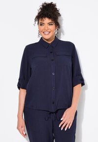 Camisa marinera de botones, con dos bolsillos en el pecho, mangas enrolladas y un dobladillo con cordón. Fabricada con un tejido ligero y de textura suave.