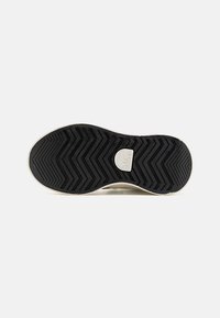 Suela de goma negra con un patrón de tracción en zigzag, que presenta un borde de color claro y suave. Incluye un logo circular cerca del talón.