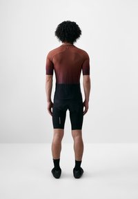 A sportos kerékpáros öltözet átmenetes barna és fekete dizájnnal rendelkezik, rövid ujjú, testhezálló sziluett és texturált anyag.