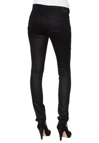 Jeans negros ajustados hechos de tejido elástico, con bolsillos traseros y una textura suave, combinados con zapatos de tacón altos negros.