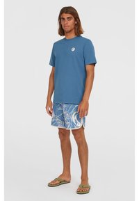 Blue cotton t-shirt with a round neckline, paired with blue patterned swim shorts and green flip-flops. Simple design; casual wear.
