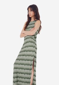 Abito lungo con motivo zigzag verde e bianco, design senza maniche con alte spaccature laterali, realizzato in tessuto leggero per una vestibilità fluida.