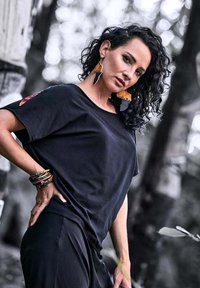 Black short-sleeve top with a relaxed fit, paired with colorful patterned bracelets and large dangling earrings featuring orange and black designs.
