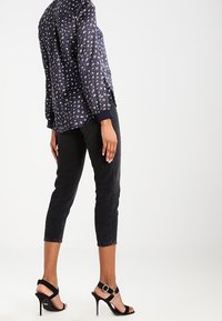 Blusa blu navy con stampa sparsa, jeans neri a vita alta, e tacchi neri con cinturino alla caviglia e hardware in argento.