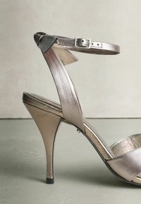Metallic silver high-heeled sandal with an ankle strap, featuring a smooth leather texture and a sleek pointed toe design.