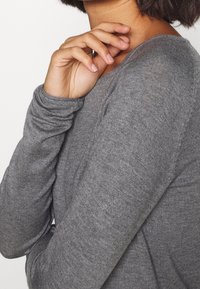 Maglietta grigia a maniche lunghe realizzata in morbido tessuto testurizzato con un design aderente e dettagli delle cuciture in vista, che mette in mostra una vestibilità rilassata attorno al braccio.