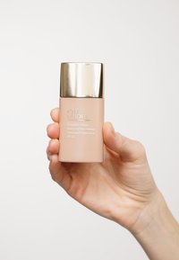 Estee Lauder Double Wear foundation i en frostet glassflaske, beige farge med gullkapsel. Tekst på flasken inkluderer produktnavn og SPF-detaljer.