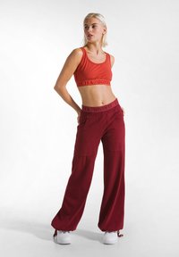 Rode crop top met een logo-band en losse, diep rode broek met Franse zakken en een trekkoord aan de onderkant. Outfit compleet met witte sneakers.