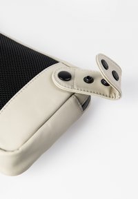 Beige en zwarte clutch met een gladde buitenkant, een gestructureerd gaasdetail en drukknoopsluiting. Heeft afgeronde hoeken en contrasterende stiksels.