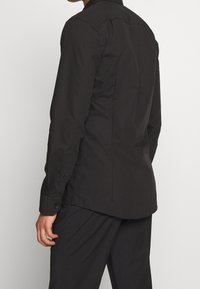 Czarna koszula z długim rękawem, zakończona spiczastym kołnierzykiem, mankietami na guziki i prostym krojem, wykonana z gładkiej, fakturowanej tkaniny, z minimalną ilością detali.