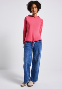 Felpa rosa con coulisse all'orlo, abbinata a jeans blu a gamba larga. La felpa ha una texture morbida, mentre il denim è sbiadito.