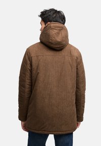 Ruskea samettinukkainen takki, jossa on suuri huppu, pystysuorat kohokuvioinnit, rento istuvuus ja helmassa päättyy lantioihin.