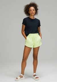 Navy t-shirt met korte mouwen, gecombineerd met lichtgroene shorts met een elastische tailleband. Draagt witte sandalen tegen een grijze achtergrond.